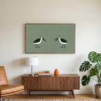 Two shorebirds art on a TV above a walnut credenza with a brass lamp and a monstera plant