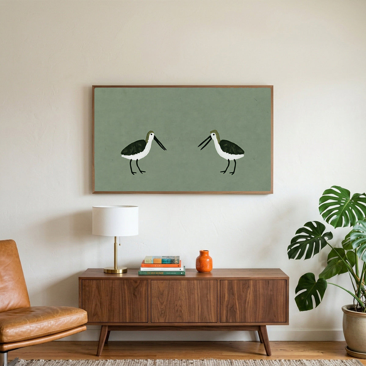 Two shorebirds art on a TV above a walnut credenza with a brass lamp and a monstera plant