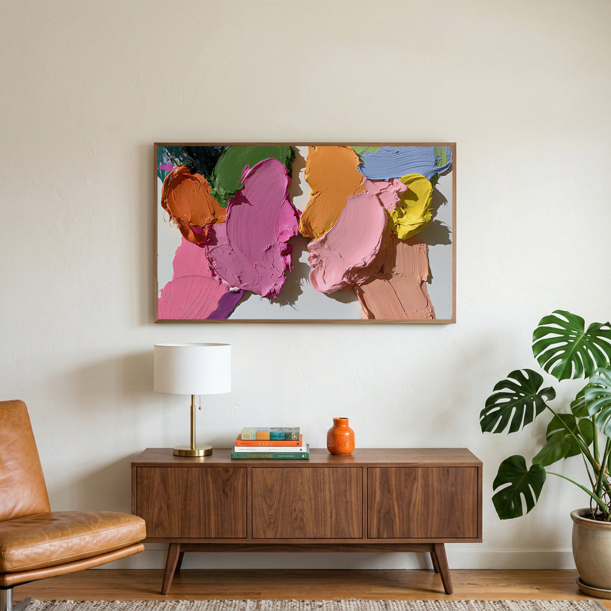 Pastel paint strokes art on a TV above a walnut credenza with a brass lamp and a monstera plant