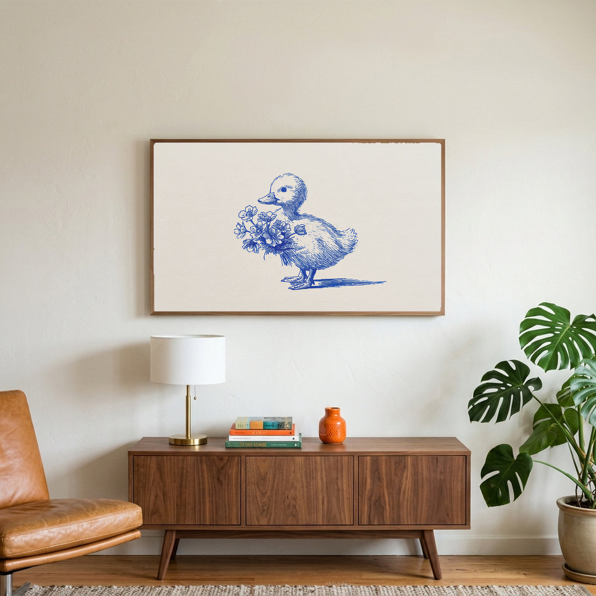 Duckling art on a TV above a walnut credenza with a brass lamp and a monstera plant