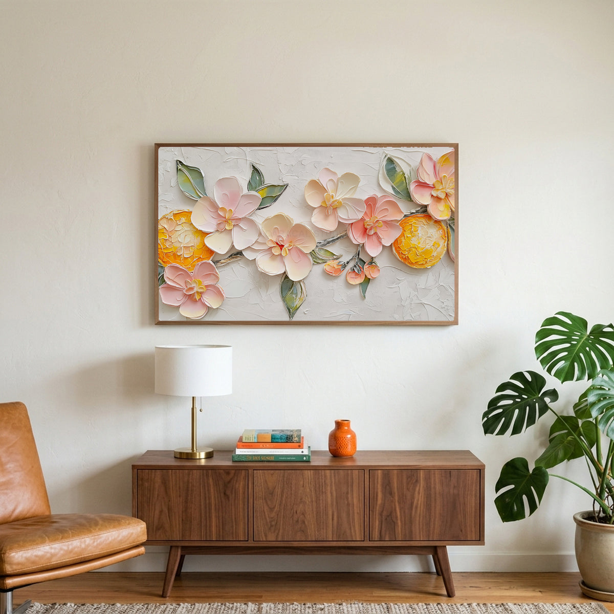 Blossom and orange art on a TV above a walnut credenza with a brass lamp and a monstera plant