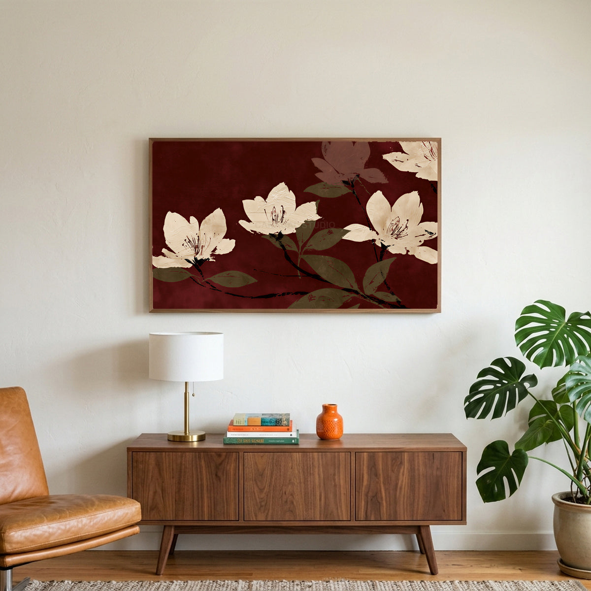 Cream blossoms on burgundy art on a TV above a walnut credenza with a brass lamp and a monstera plant
