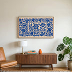 Blue paper cut flowers art on a TV above a walnut credenza with a brass lamp and a monstera plant