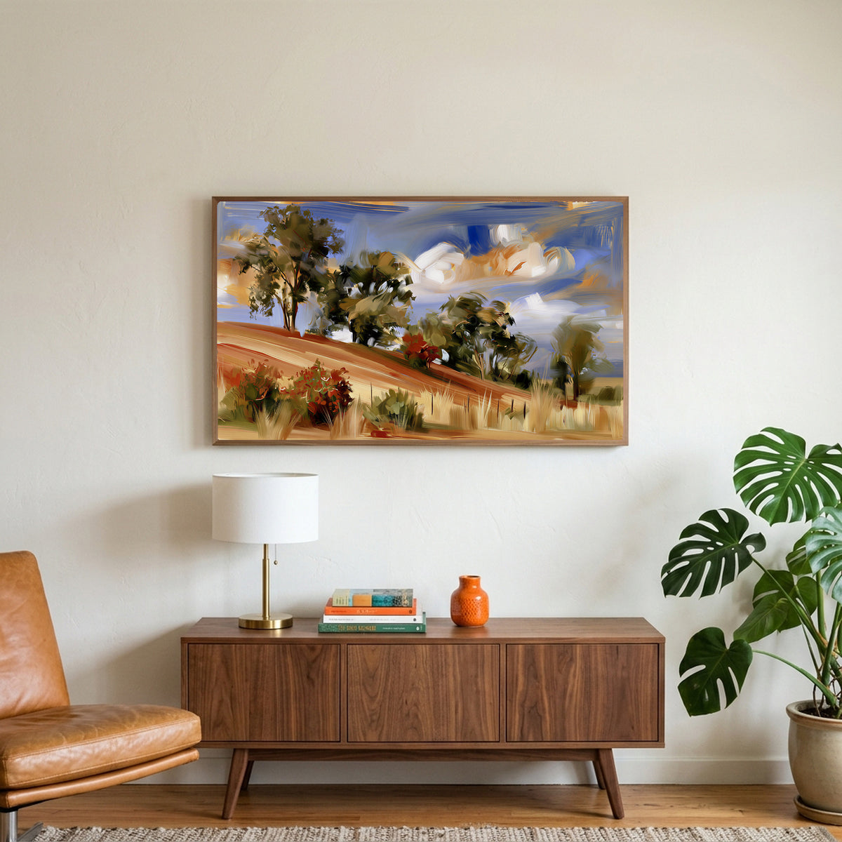 Hillside trees art on a TV above a walnut credenza with a brass lamp and a monstera plant