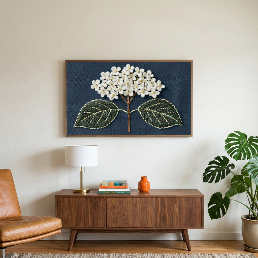 Embroidered hydrangea art on a TV above a walnut credenza with a brass lamp and a monstera plant