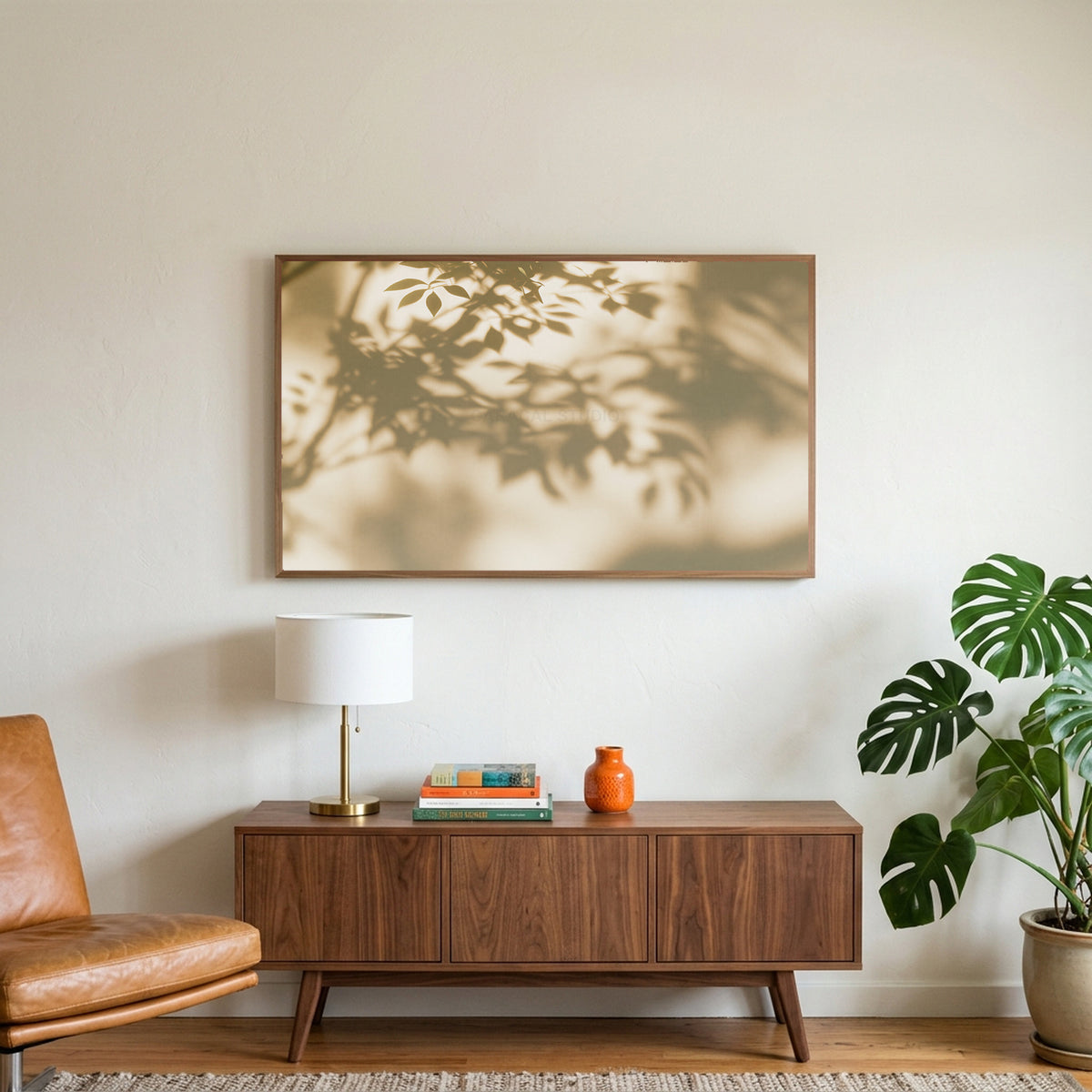 Leaf shadow art on a TV above a walnut credenza with a brass lamp and a monstera plant