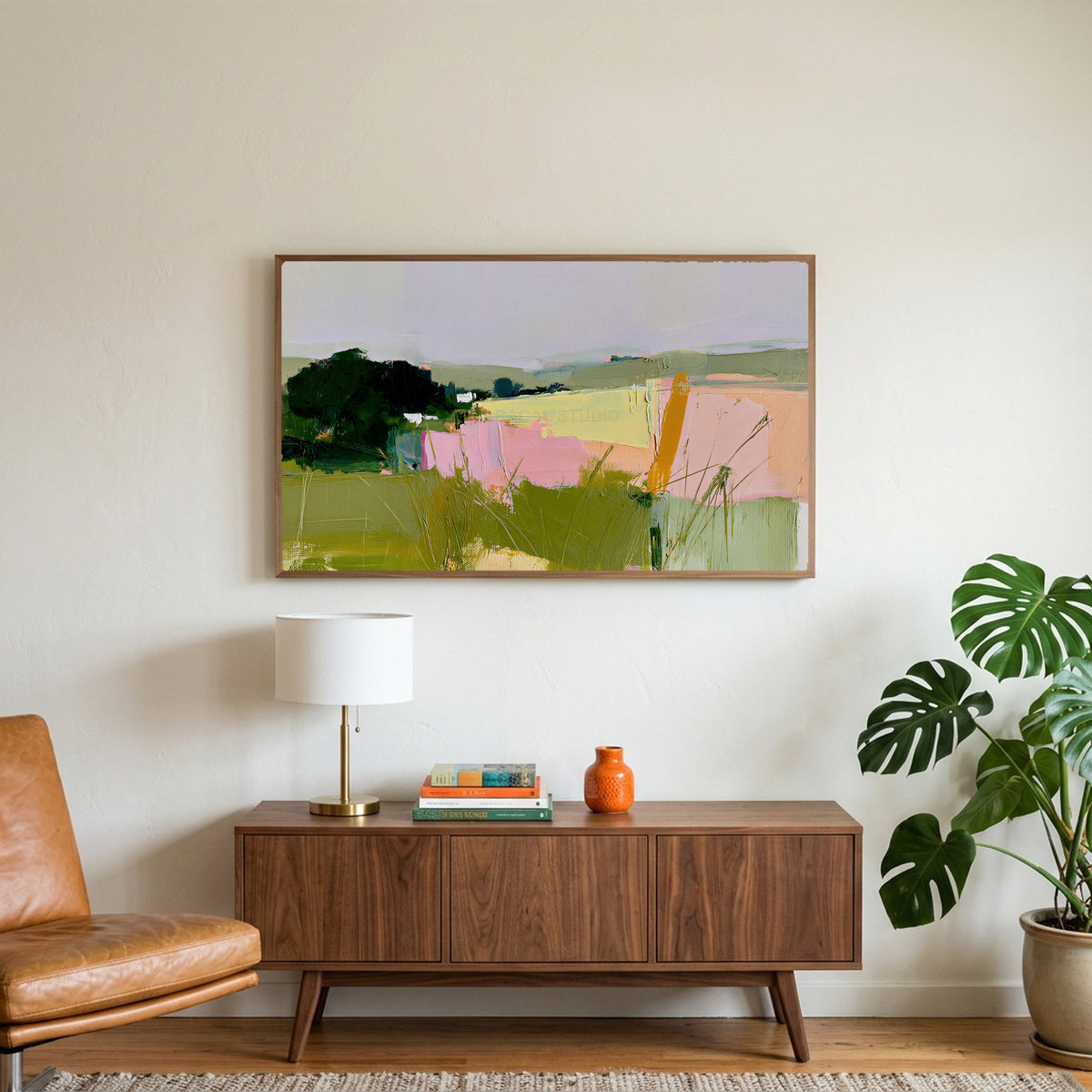 Abstract countryside art on a TV above a walnut credenza with a brass lamp and a monstera plant