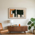 Minimalist black cow art on a TV above a walnut credenza with a brass lamp and a monstera plant
