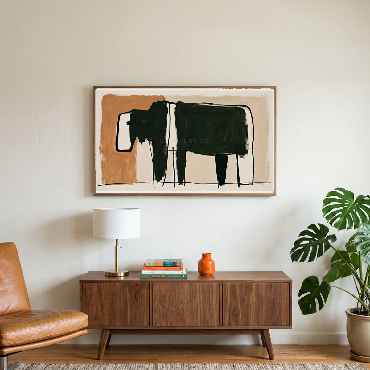 Minimalist black cow art on a TV above a walnut credenza with a brass lamp and a monstera plant