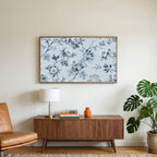Toile wild roses art on a TV above a walnut credenza with a brass lamp and a monstera plant