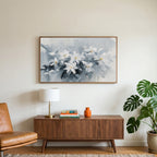 White flower art on a TV above a walnut credenza with a brass lamp and a monstera plant