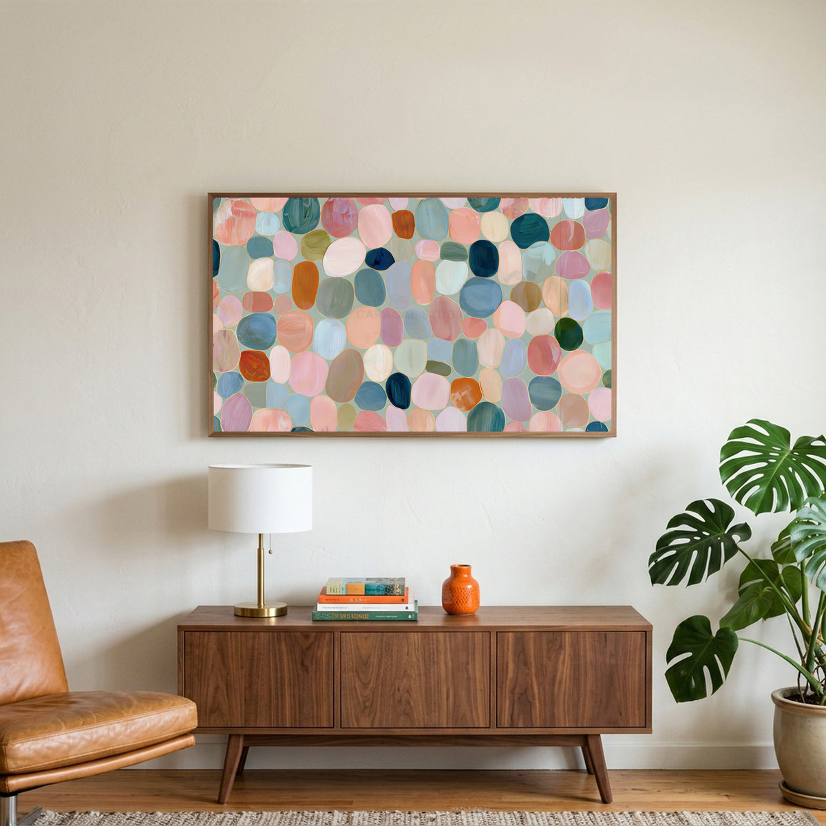 Pastel pebble mosaic art on a TV above a walnut credenza with a brass lamp and a monstera plant