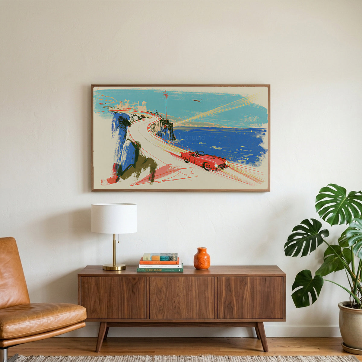 Red car on a coastal road art on a TV above a walnut credenza with a brass lamp and a monstera plant