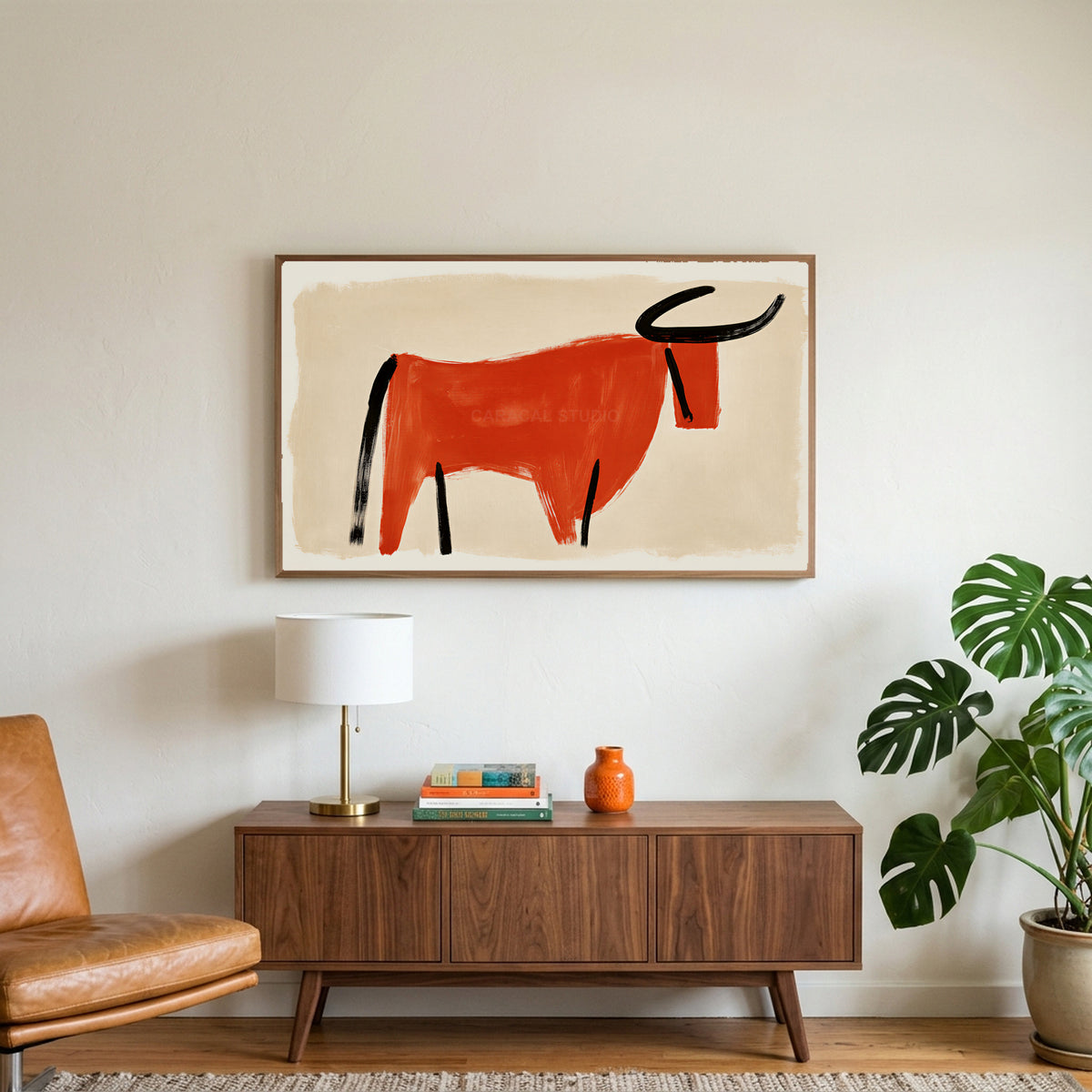 Minimalist bull art on a TV above a walnut credenza with a brass lamp and a monstera plant