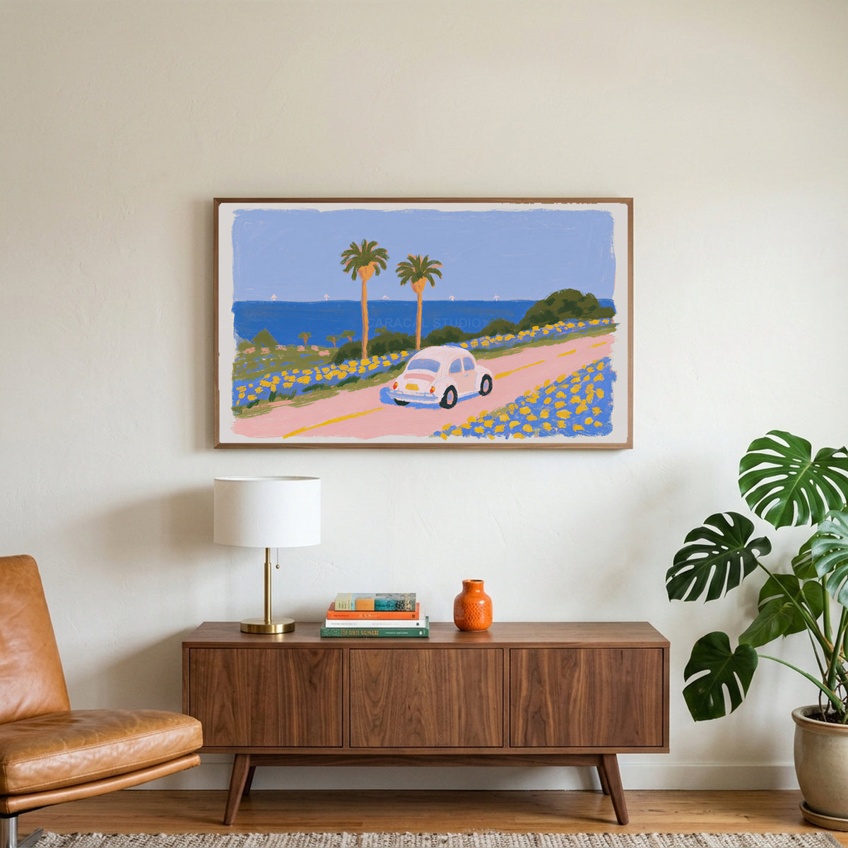 Seaside car art on a TV above a walnut credenza with a brass lamp and a monstera plant