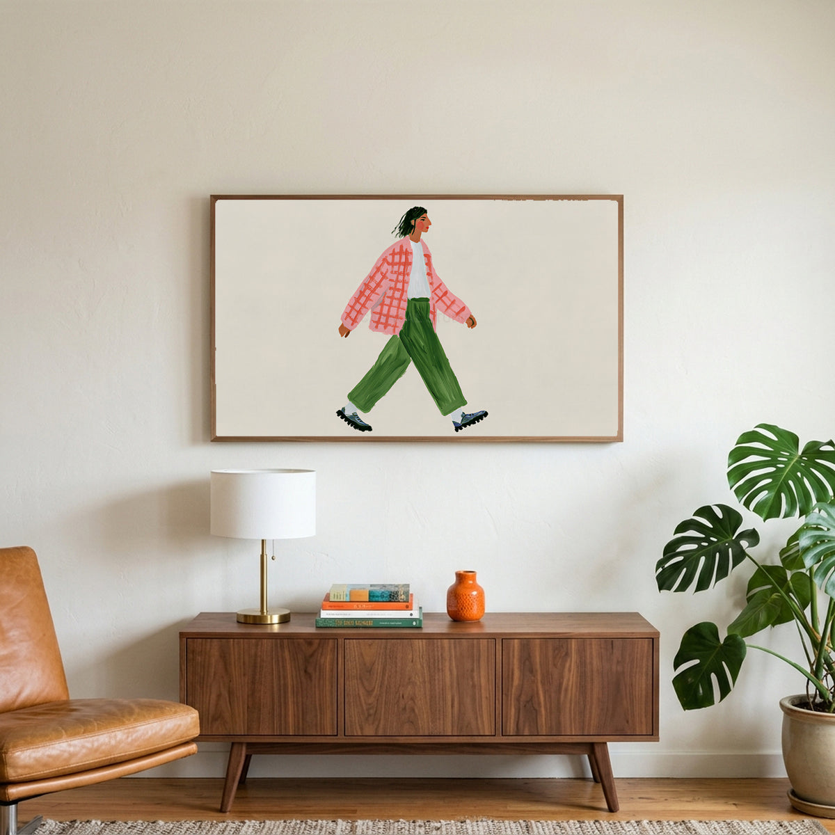 Woman walking art on a TV above a walnut credenza with a brass lamp and a monstera plant