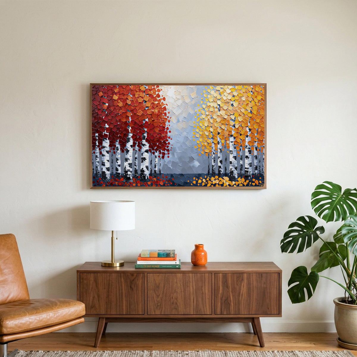 Autumn birch trees art on a TV above a walnut credenza with a brass lamp and a monstera plant