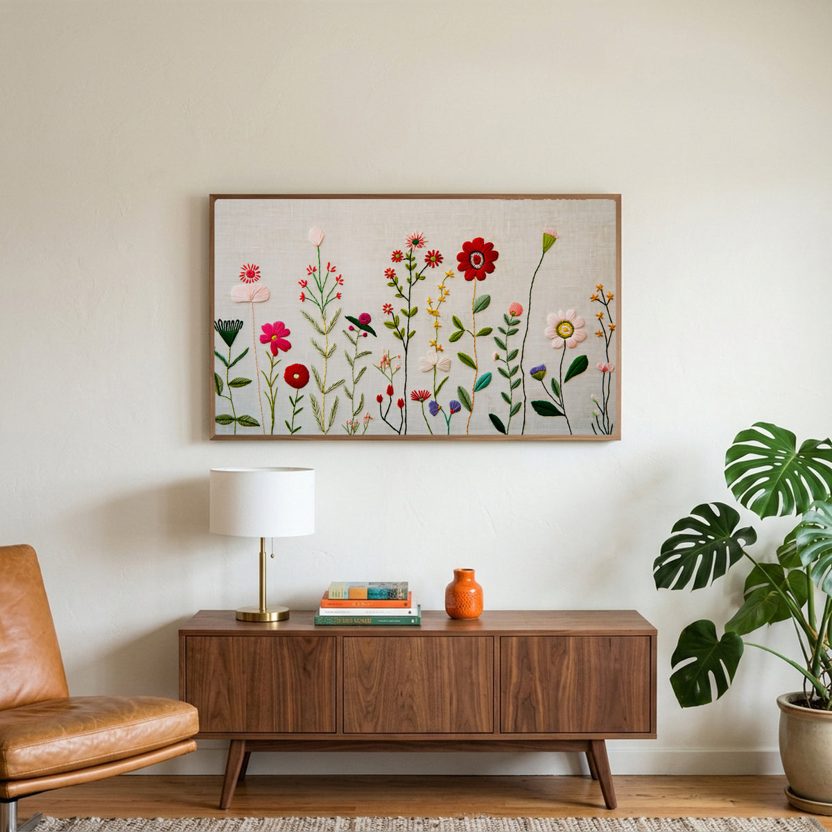 Embroidery style wildflower art on a TV above a walnut credenza with a brass lamp and a monstera plant