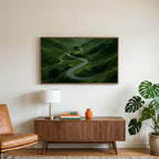 Winding road landscape art on a TV above a walnut credenza with a brass lamp and a monstera plant
