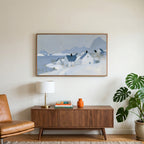 Snowy seaside village art on a TV above a walnut credenza with a brass lamp and a monstera plant