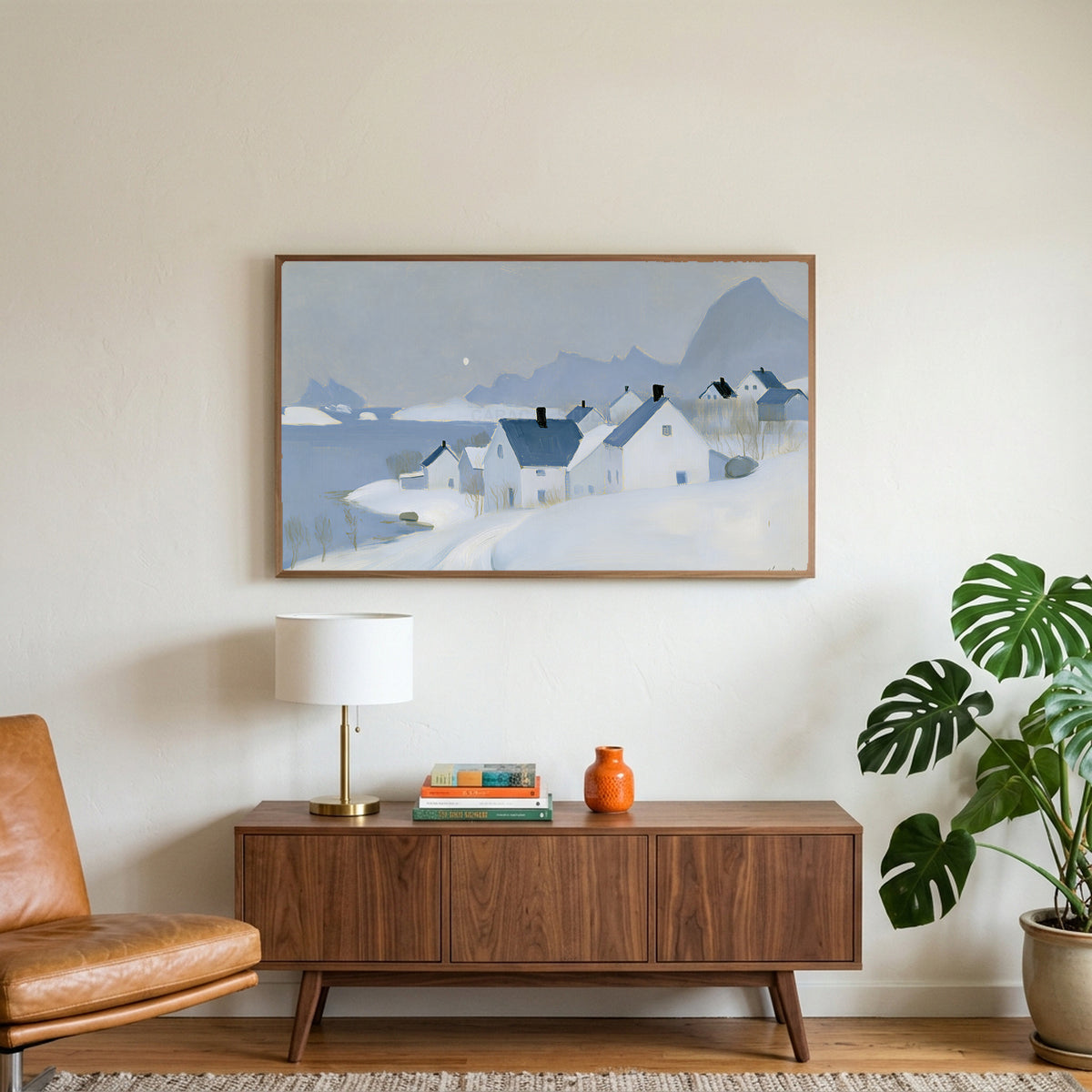 Snowy seaside village art on a TV above a walnut credenza with a brass lamp and a monstera plant