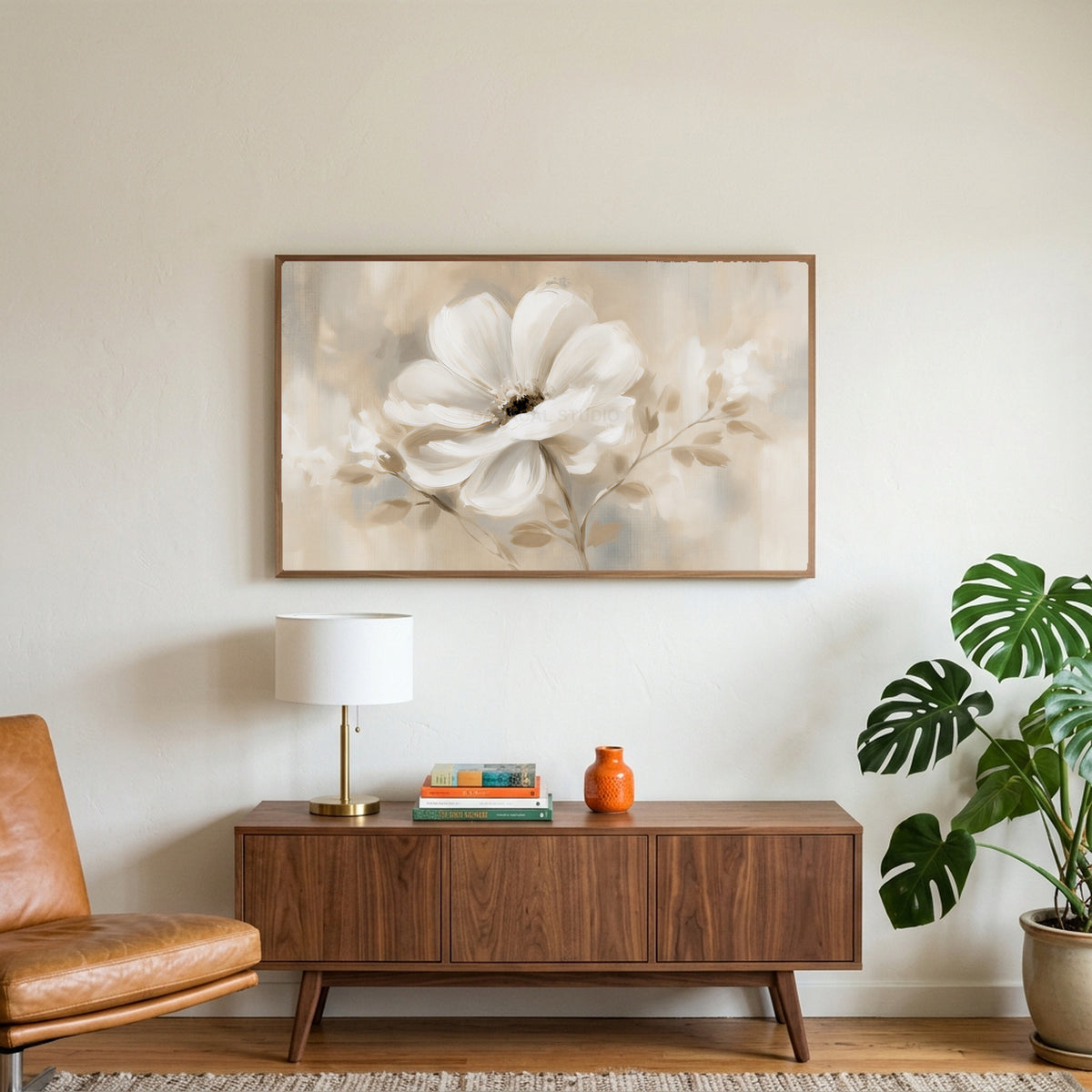 White flower art on a TV above a walnut credenza with a brass lamp and a monstera plant