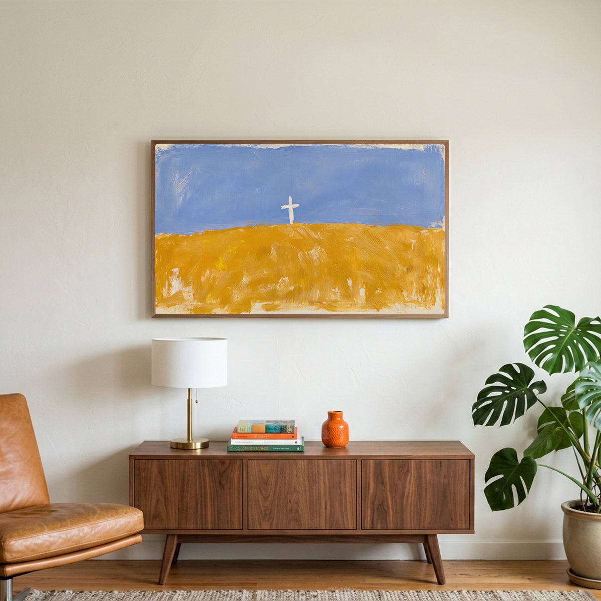 Cross on a golden field art on a TV above a walnut credenza with a brass lamp and a monstera plant