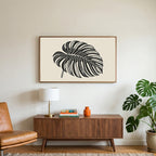 Monstera leaf art on a TV above a walnut credenza with a brass lamp and a monstera plant