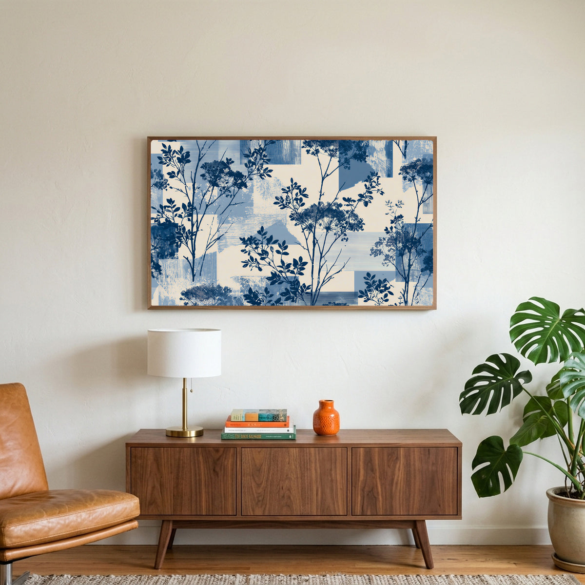 Blue botanical art on a TV above a walnut credenza with a brass lamp and a monstera plant