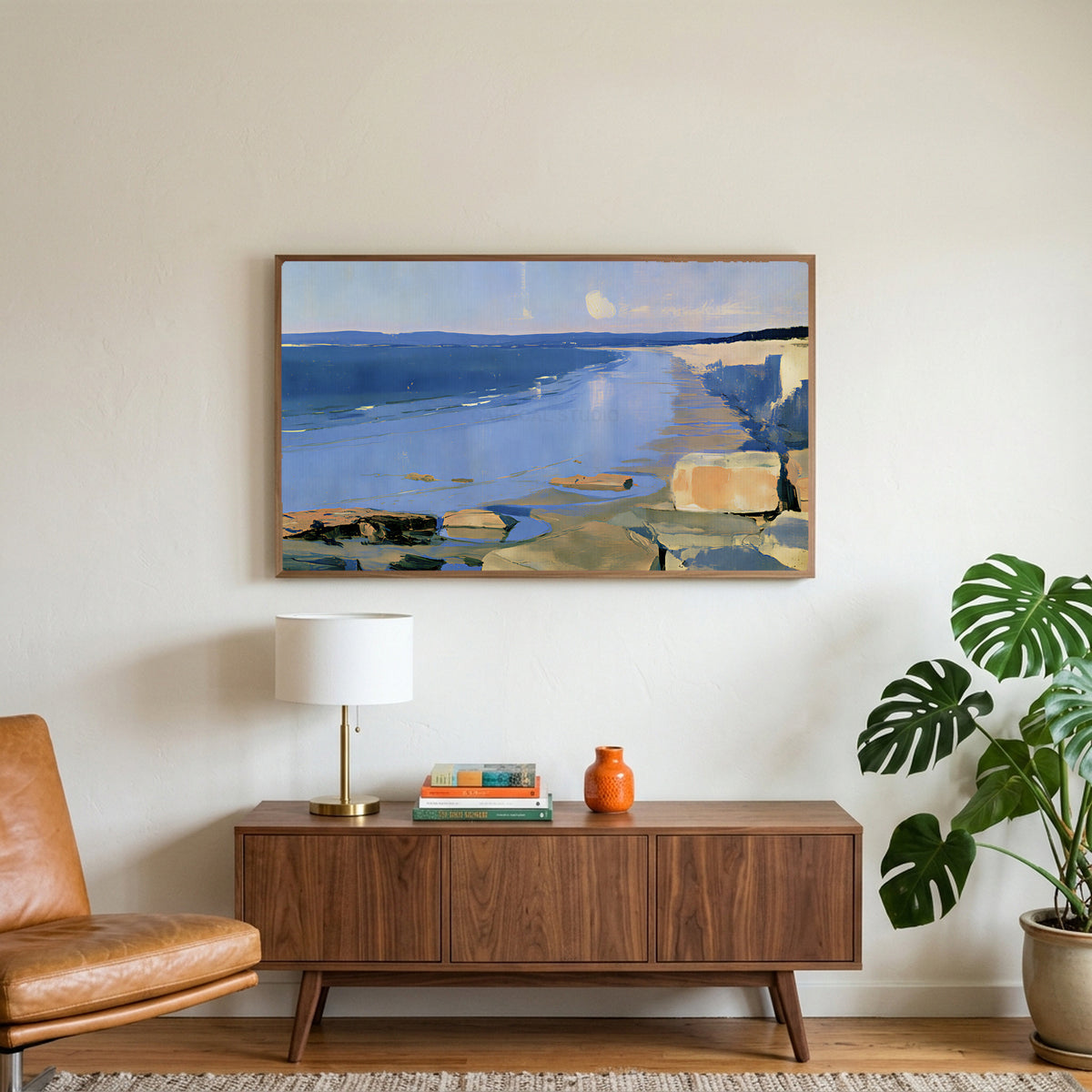 Low tide beach and cliffs art on a TV above a walnut credenza with a brass lamp and a monstera plant