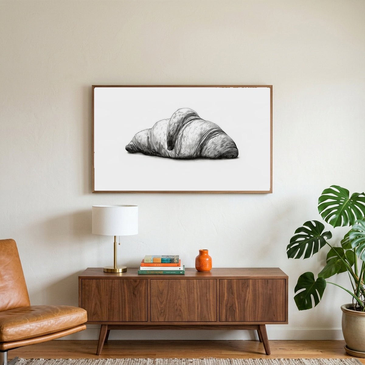 Croissant etching art on a TV above a walnut credenza with a brass lamp and a monstera plant